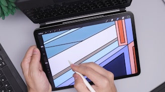 A person is holding a tablet with a stylus, creating a geometric abstract design. The tablet screen shows a digital drawing application with a user interface visible. The background includes part of a laptop keyboard and a green plant in the corner.
