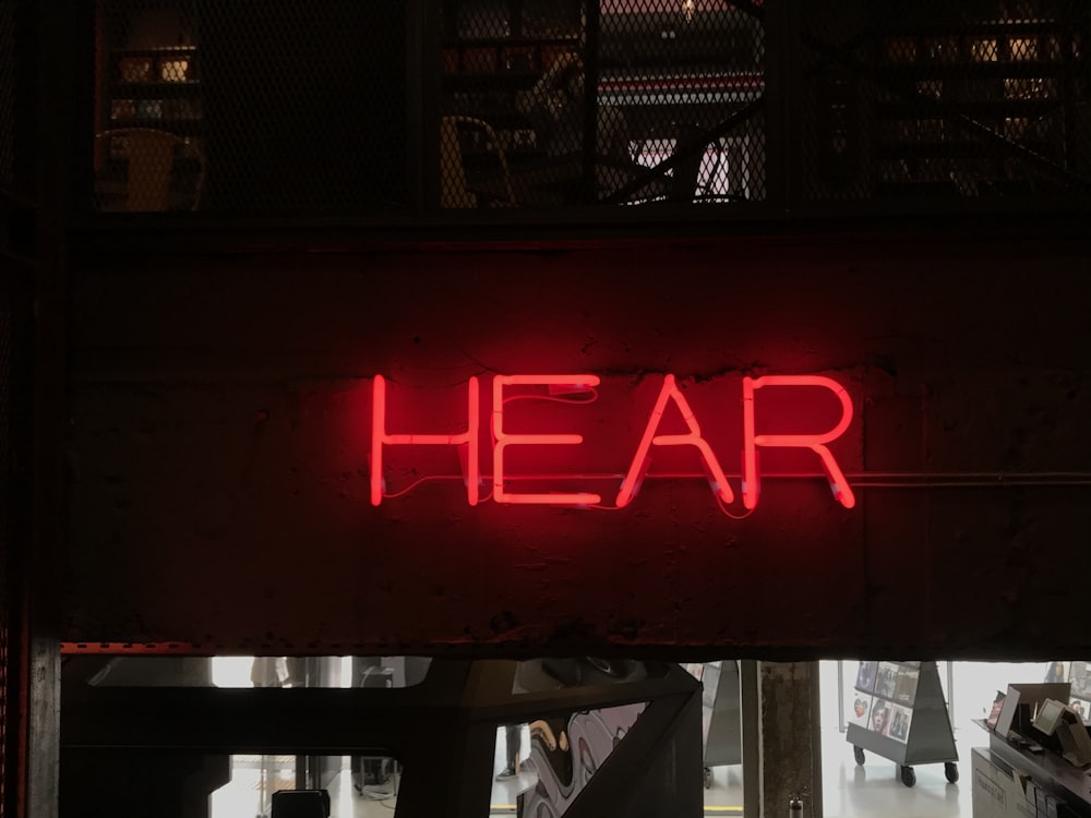 a red neon sign that reads hear above a doorway