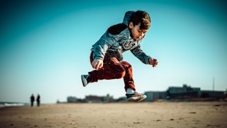 boy in blue jacket and red pants jumping on brown field during daytime