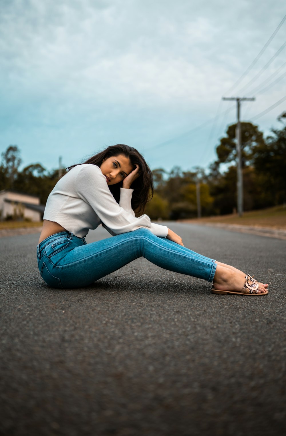 woman in white long sleeve shirt and blue denim jeans sitting on road during daytime