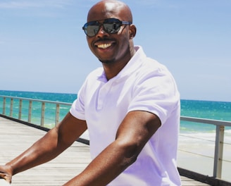 man in white polo shirt wearing sunglasses sitting on brown wooden dock during daytime