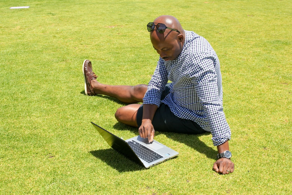 푸른 잔디밭에 앉아 파란색과 흰색 체크 무늬 버튼 업 셔츠를 입은 남자
