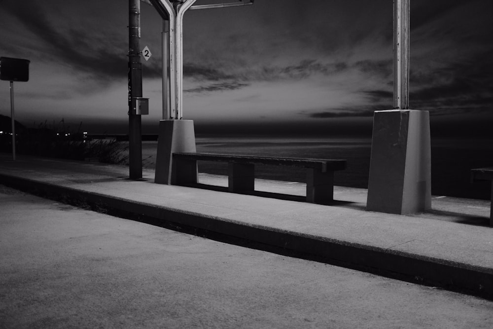 grayscale photo of wooden bench near body of water