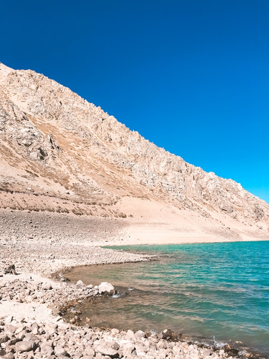 brown mountain near body of water during daytime in Embalse el Yeso Chile