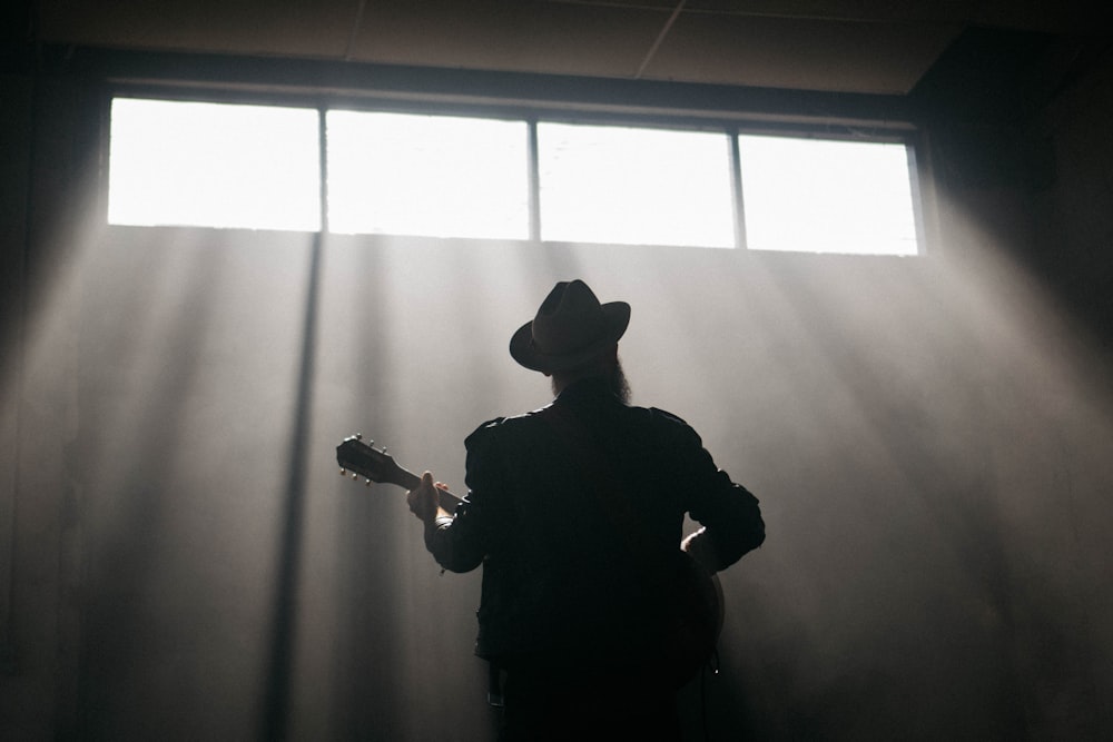 man in black jacket and black hat standing near window