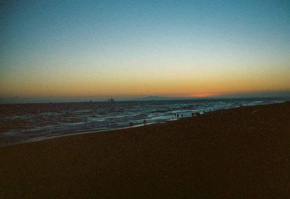 the sun is setting over the ocean and people are walking on the beach