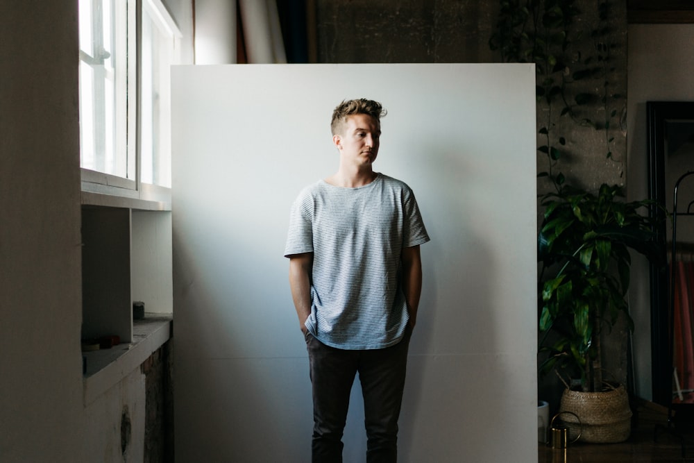 man in gray crew neck t-shirt standing beside white wall