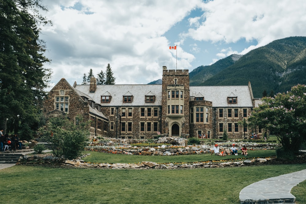 brown concrete building near green grass field and mountain under white clouds and blue sky during