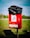 A red outdoor waste bin situated on a grassy area, with a black plastic bag lining the top. The bin features a sign illustrating a person disposing of waste alongside a dog, indicating it is for dog waste. The background is slightly blurred, showing green trees and a blue sky.