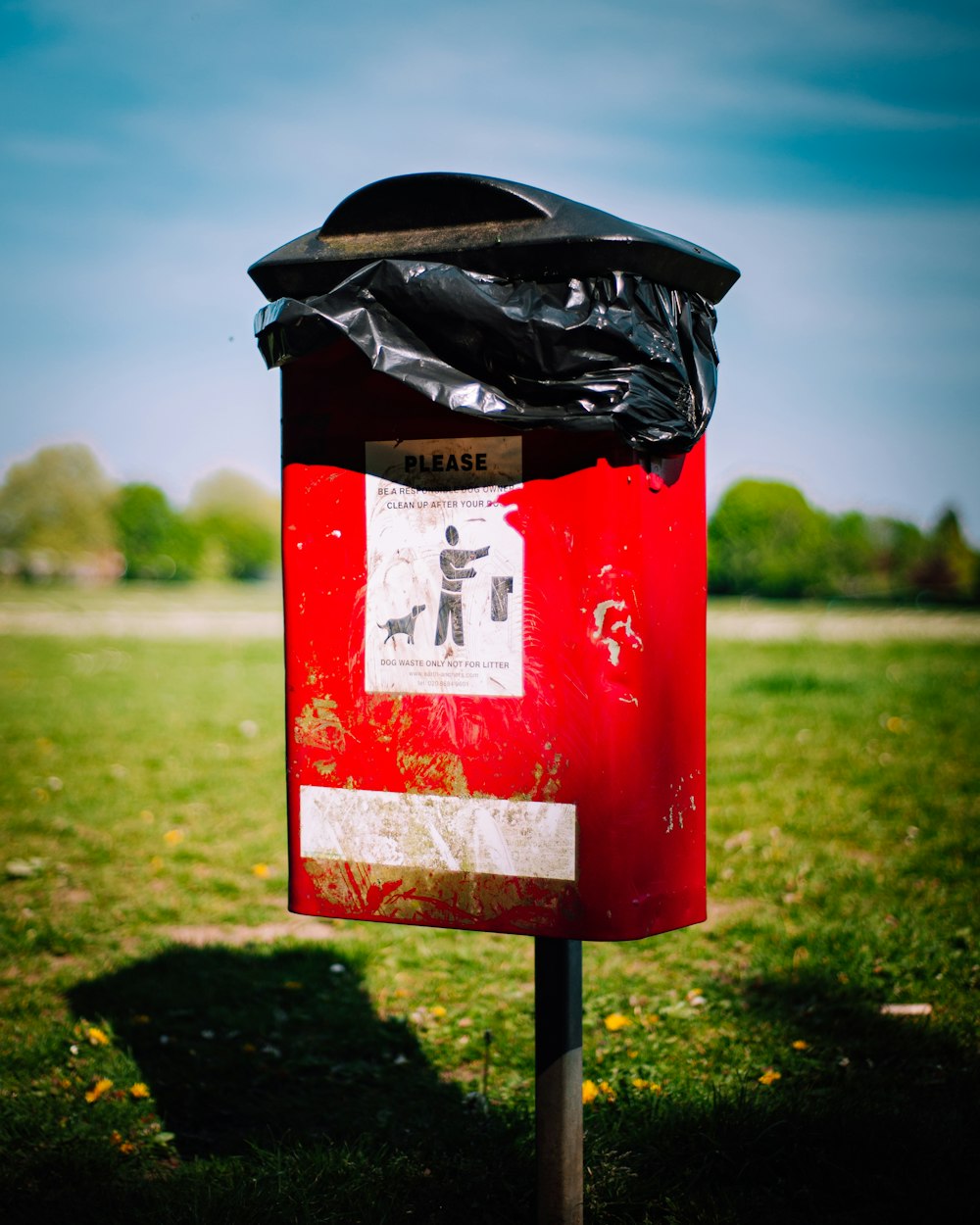 red and black trash bin on green grass field during daytime
