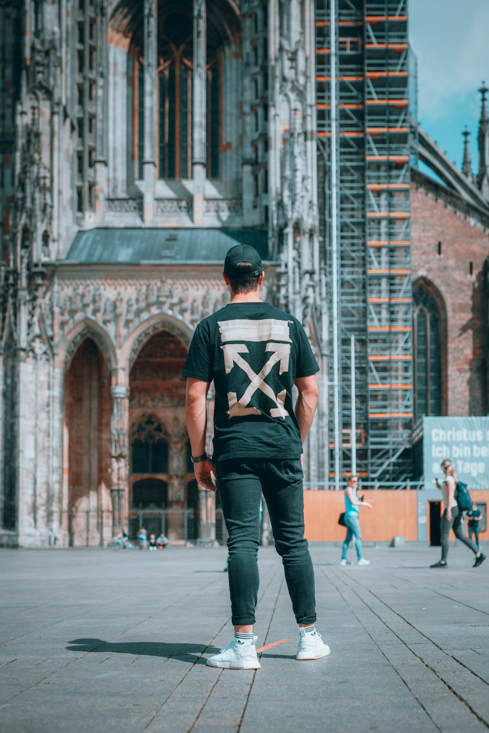 man in black and white t-shirt and blue denim jeans standing on sidewalk during daytime