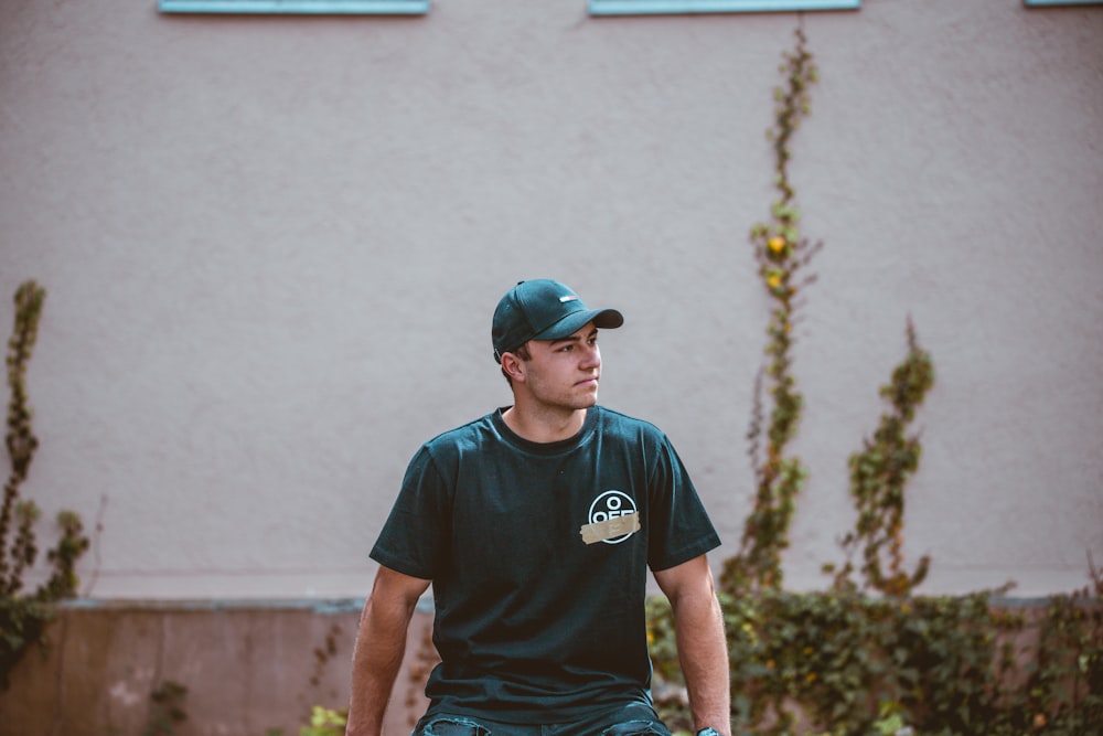 Mann in grünem Rundhals-T-Shirt und blauer taillierter Mütze in der Nähe der weißen Wand während