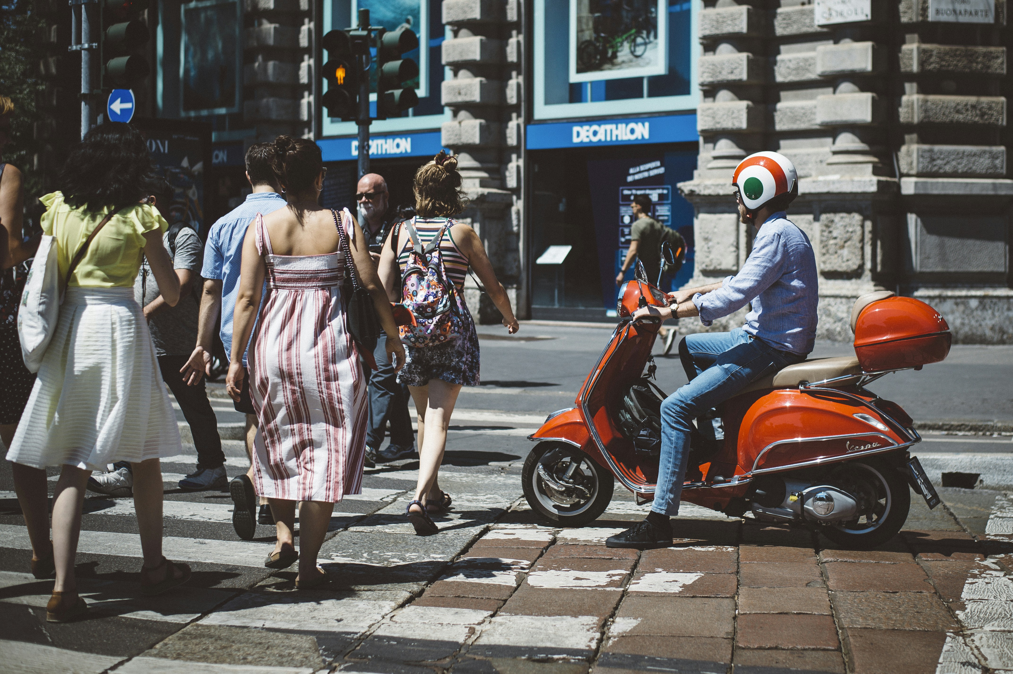 A young man on a scooter passes tourists at a pedestrian crossing. Milan.
