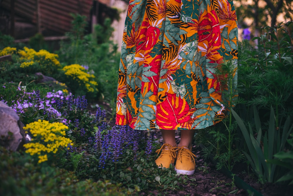 낮 동안 노란 꽃밭에 서 있는 주황색과 파란색 꽃 드레스를 입은 여자