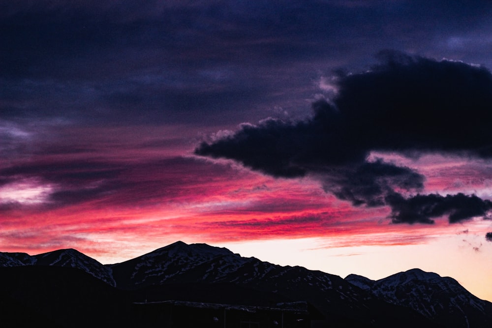 black and brown mountains under orange and gray cloudy sky