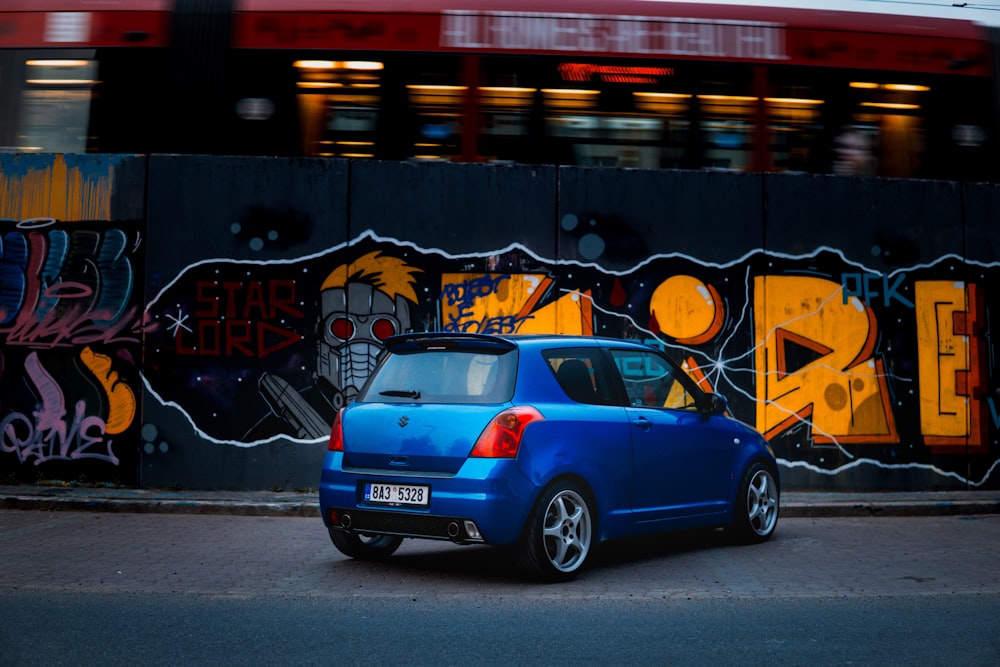blue volkswagen beetle parked beside wall with graffiti