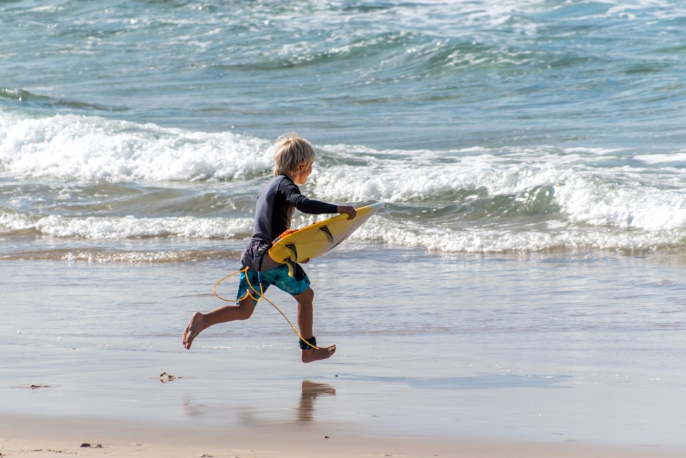 woman in blue and black wet suit carrying yellow surfboard walking on beach during daytime