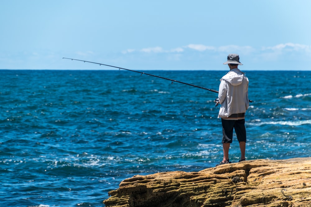 man in white shirt and black shorts fishing on sea during daytime