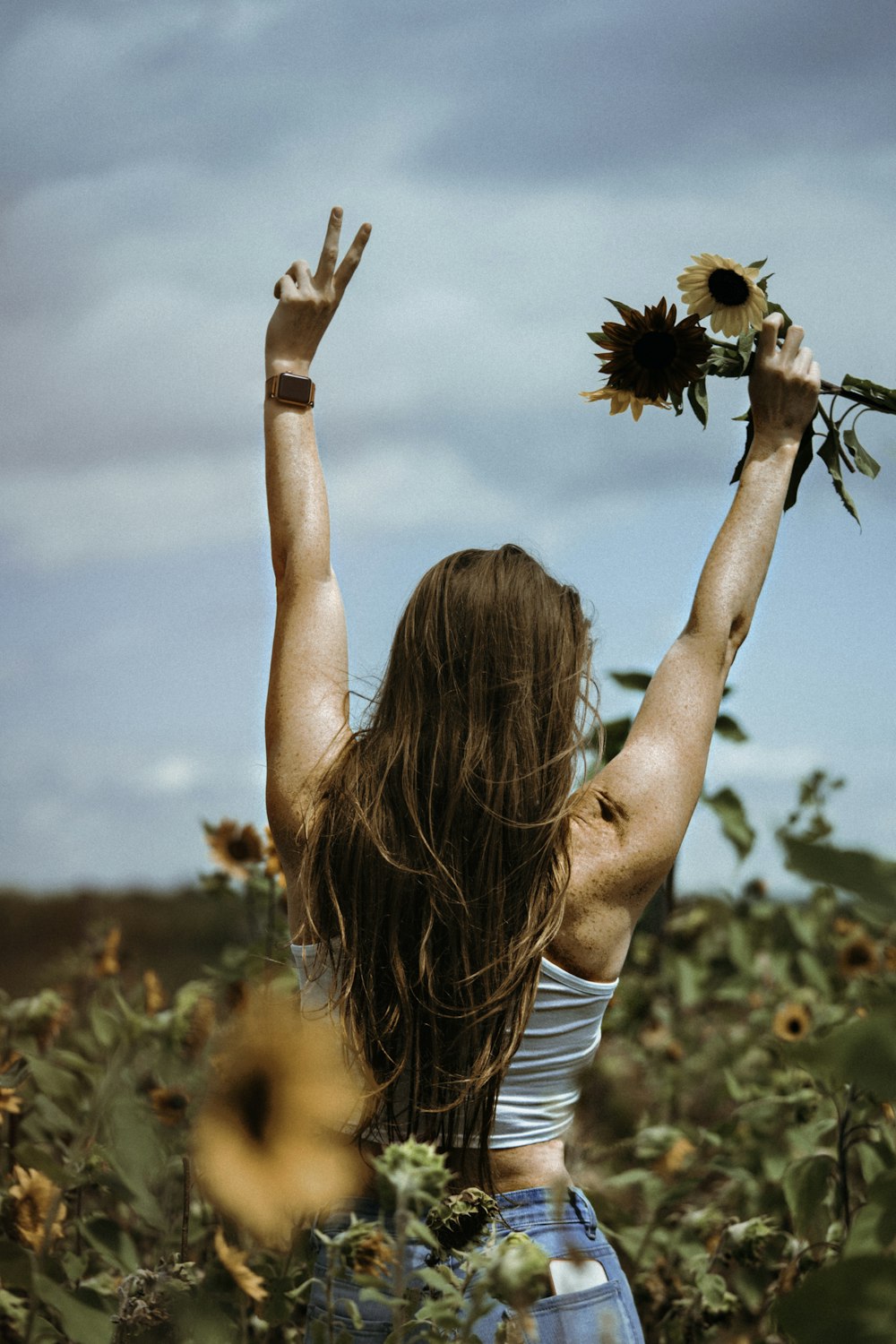 woman in white tank top holding sunflower during daytime