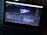 A laptop displays an open software program, likely a video editing or motion graphics application, showing multiple layers and a timeline with a preview of a logo in the center of the screen. The environment is dimly lit, highlighting the screen's glow.