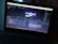 A laptop displays an open software program, likely a video editing or motion graphics application, showing multiple layers and a timeline with a preview of a logo in the center of the screen. The environment is dimly lit, highlighting the screen's glow.