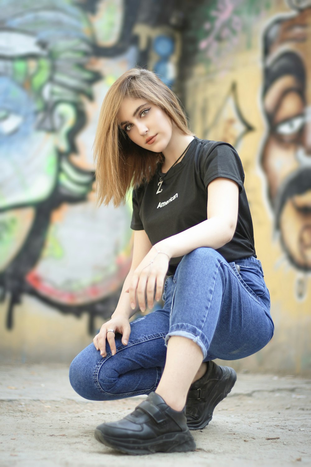 黒いシャツとブルーデニムのジーンズを着た女性がコンクリートの床に座っている