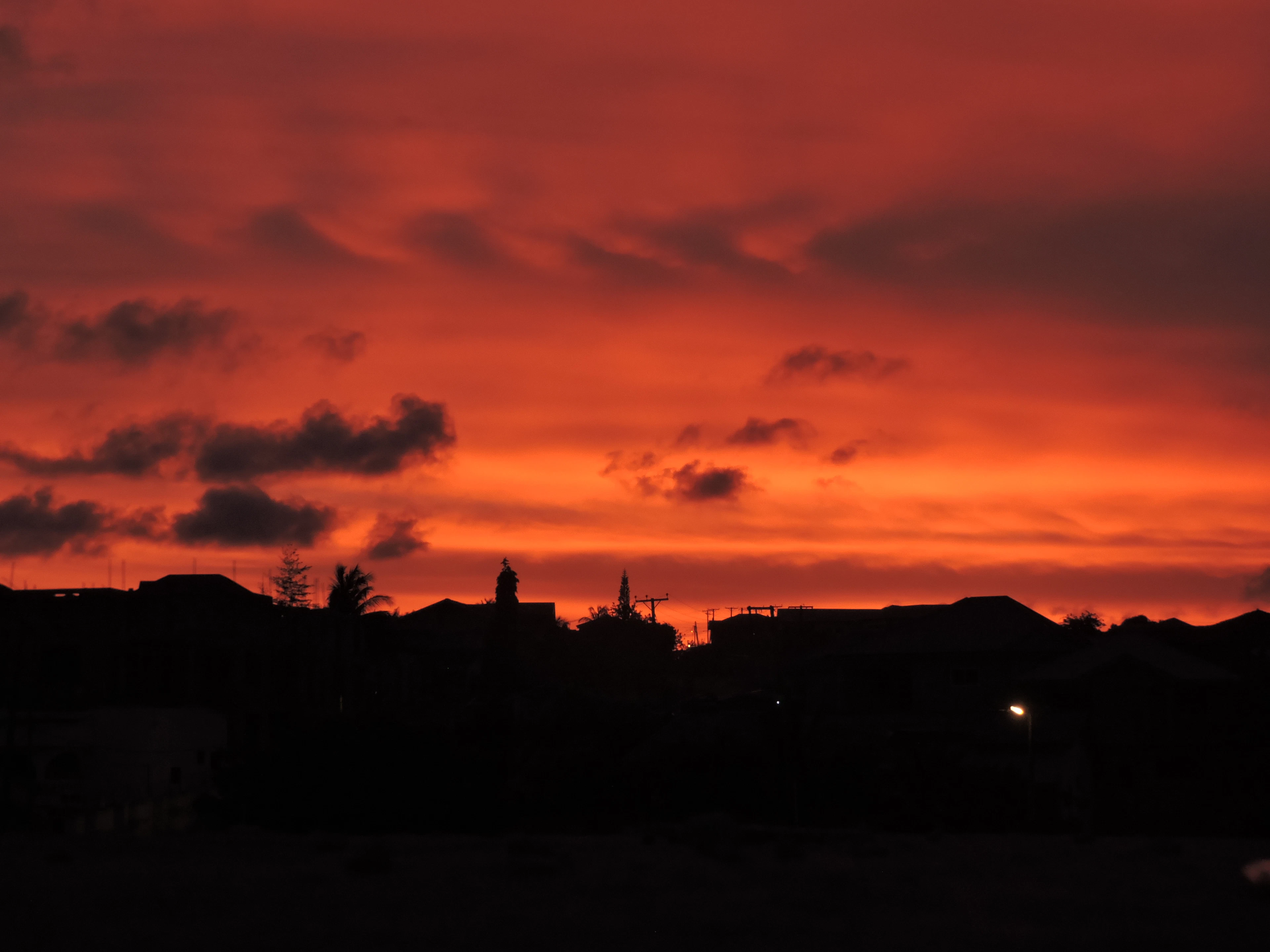 A fiery orange-red sunset glows over the silhouetted rooftops of the city skyline.
