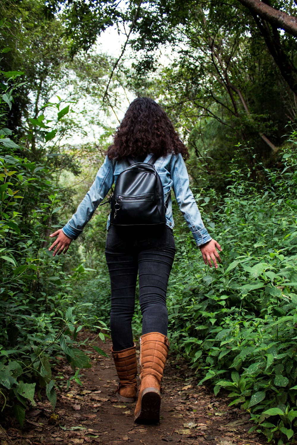 Mujer con camisa negra de manga larga y pantalones negros caminando por el bosque durante el día