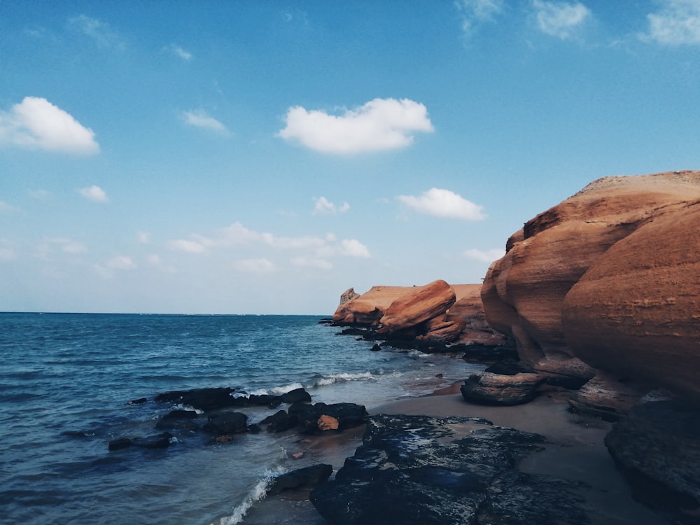 brown rock formation on sea under blue sky during daytime