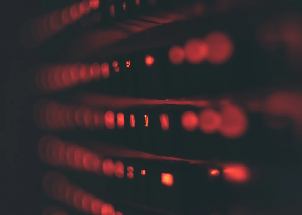 A dark silhouette of a person in a hoodie standing in front of glowing blue server racks.