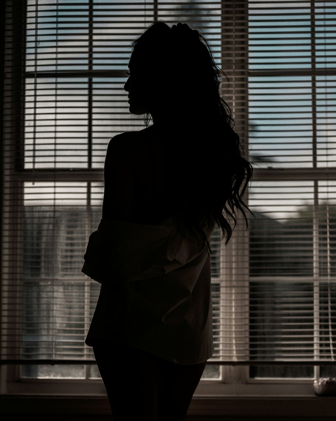 woman in white dress standing near window blinds