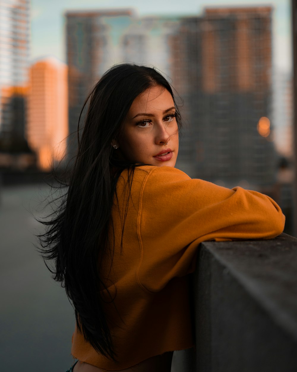 woman in orange hoodie leaning on concrete wall during daytime