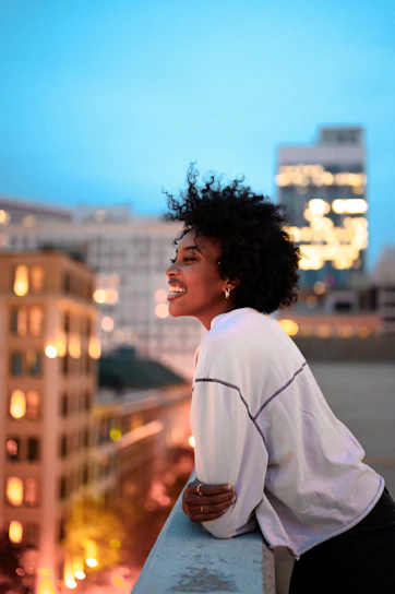 A woman with curly hair leaning on a rooftop railing overlooking a city