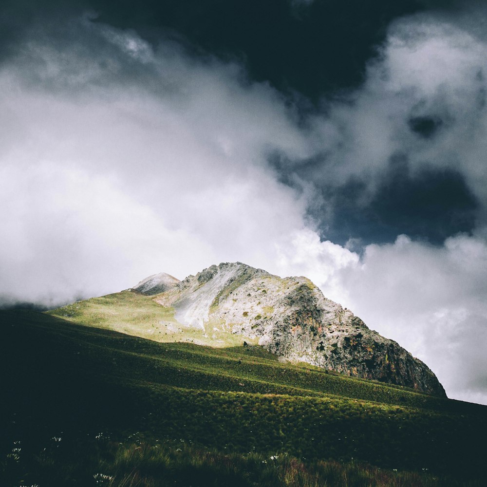 green grass field near snow covered mountain under cloudy sky during daytime