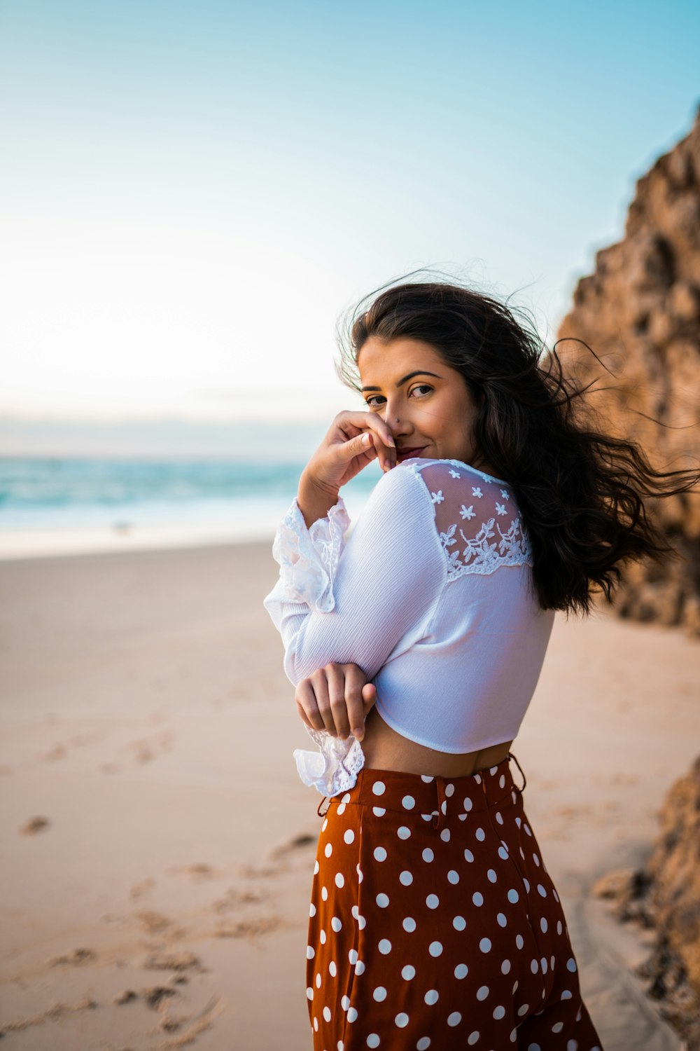 girl in white long sleeve shirt and black and white polka dot skirt standing on beach