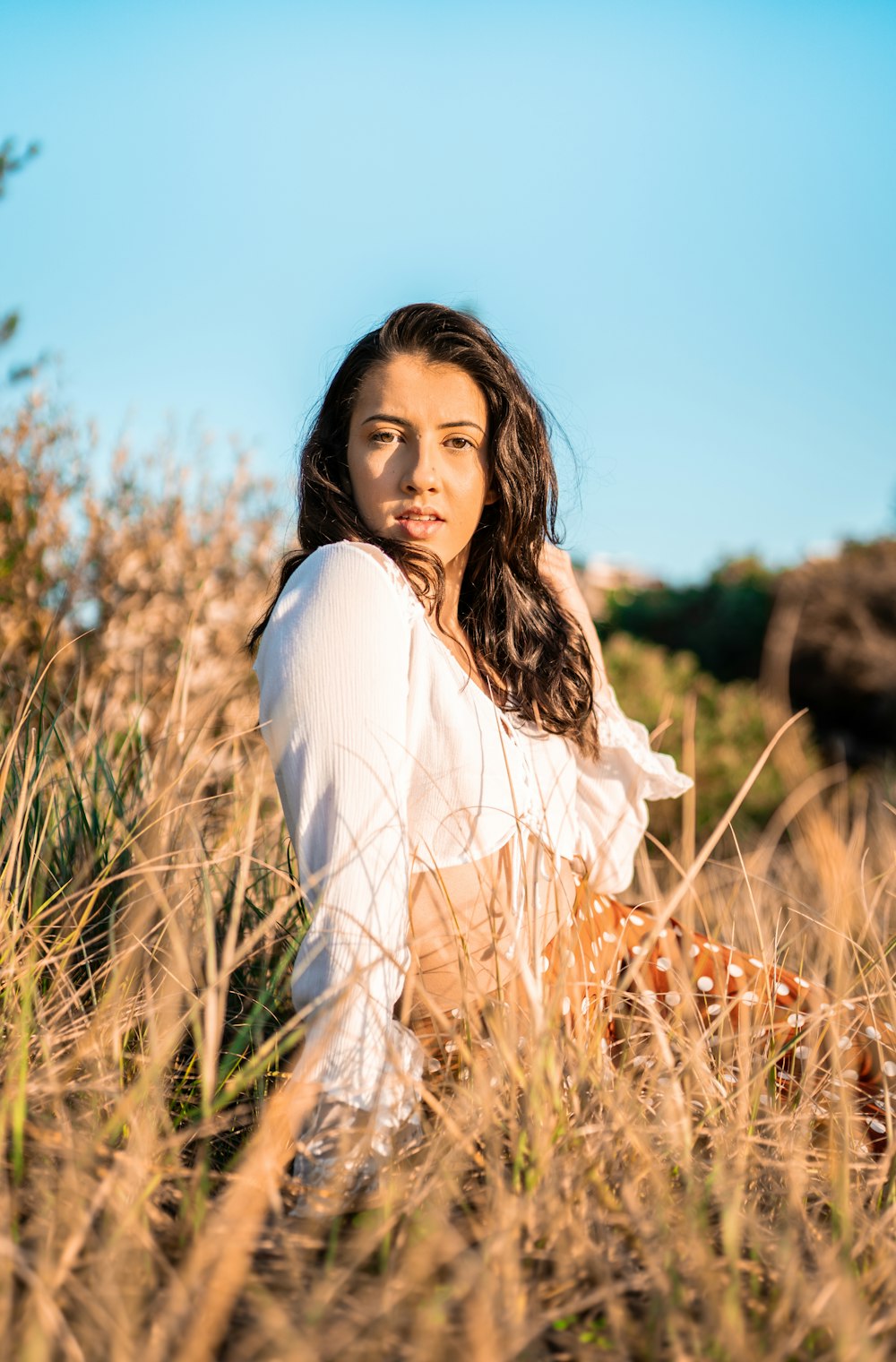 Femme en chemise blanche à manches longues debout sur le champ d’herbe brune pendant la journée