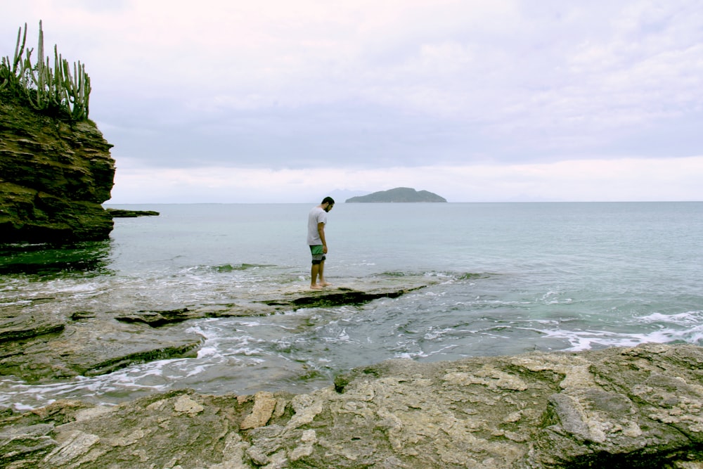 man in white shirt standing on rock by the sea during daytime