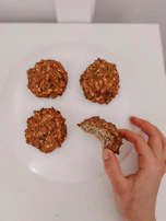 A hand holding a perfectly round oatmeal cookie with visible oats and raisins.