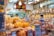 A traditional shop selling various dried goods, with shelves full of jars and containers. Two men interact in the brightly lit store, surrounded by an array of packaged products and handwritten signs displaying prices. Hanging light bulbs add a warm glow to the bustling environment.
