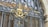 An intricately designed wrought iron gate with golden decorative elements and floral motifs is positioned in front of a window. The metalwork features elegant swirls and ornamental details, blending classic and decorative styles.