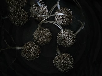 A collection of metallic scrubbers attached to transparent flexible tubing. The scrubbers have a spherical shape formed by tightly coiled metal wires, set against a dark background.