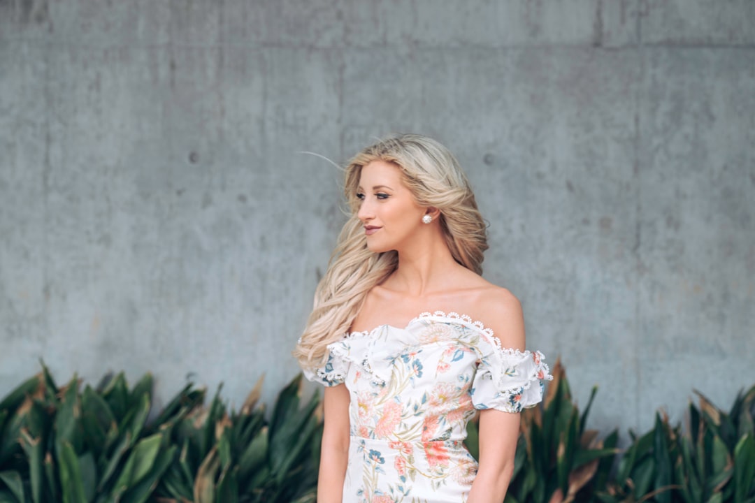 woman in white floral off shoulder dress standing beside green plants