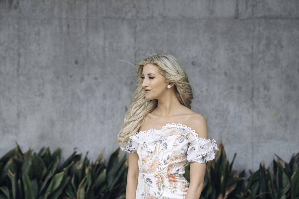 woman in white floral off shoulder dress standing beside green plants