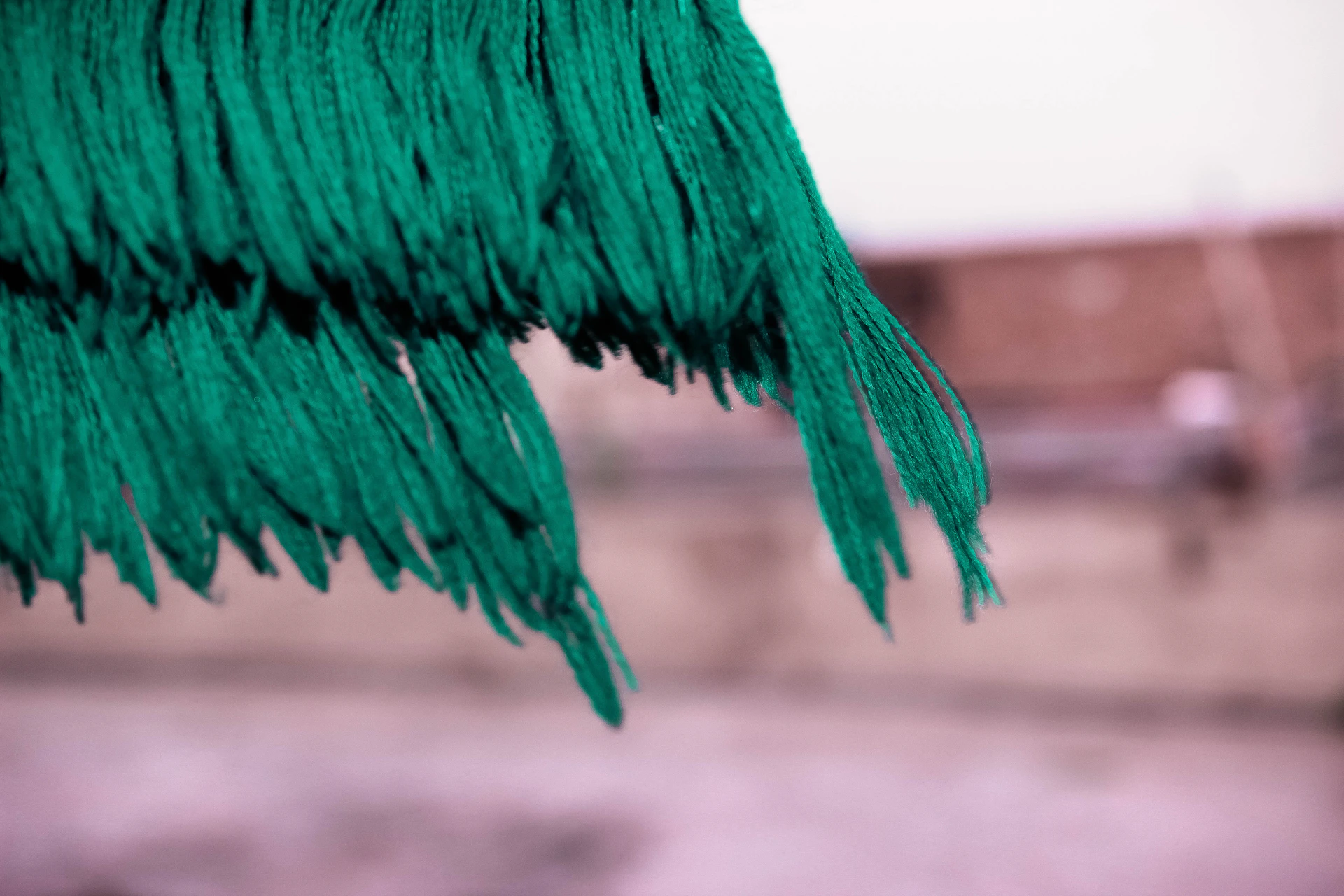 Close-up of chunky yarn being woven into a textured wall hanging, showcasing rich moss green and burnt orange tones.