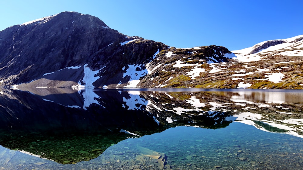 snow covered mountain near lake during daytime