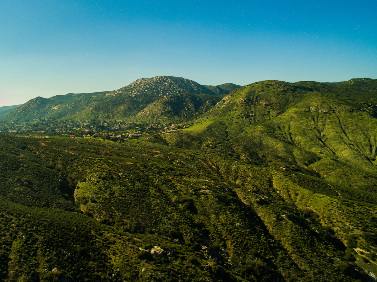 A rocky peak above green hills and scattered houses near Ramona, under a clear sky