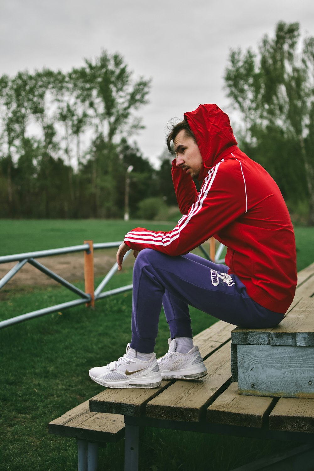 woman in red hoodie and blue pants sitting on brown wooden bench during daytime