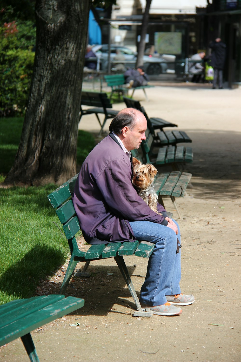 Homme en pull marron et jean bleu assis sur un banc en métal vert