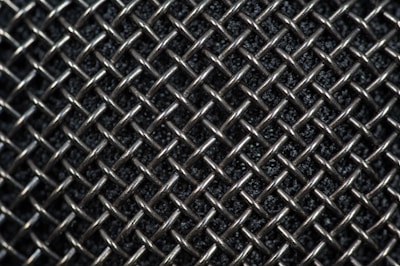 A close-up view of a metallic mesh pattern with interwoven wires forming a grid-like structure. The background appears dark, highlighting the reflective quality of the silver-colored metal.