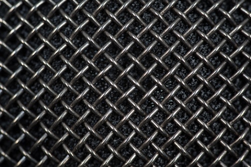 A close-up view of a metallic mesh pattern with interwoven wires forming a grid-like structure. The background appears dark, highlighting the reflective quality of the silver-colored metal.